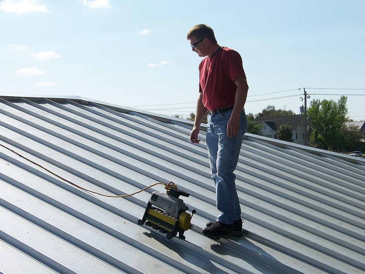Worker operating roof seamer machine on standing seam metal roof